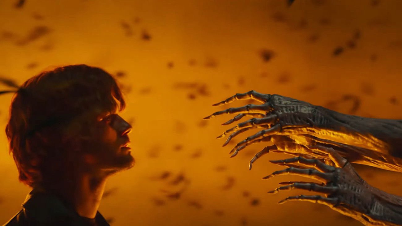 Terror em Silent Hill – Regresso Para o Inferno: homem em perfil encara mãos monstruosas sob luz laranja, em cena de ameaça sobrenatural.