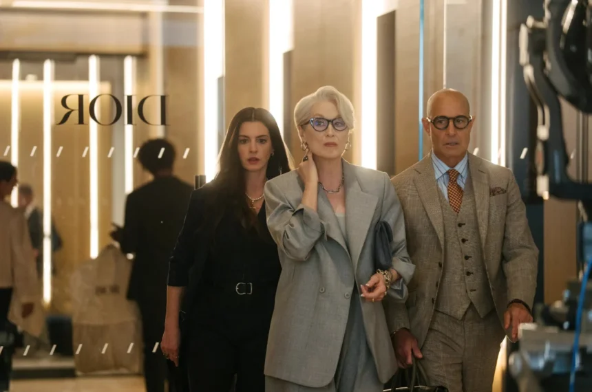 Anne Hathaway, Meryl Streep e Stanley Tucci caminhando em um ambiente de luxo com o logotipo da Dior ao fundo em "O Diabo Veste Prada 2".