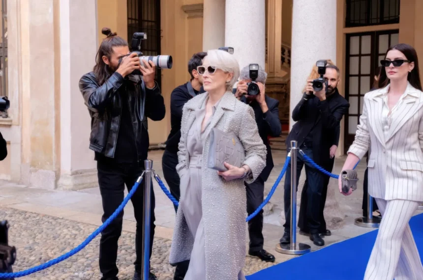 Meryl Streep e Anne Hathaway caminham em um tapete azul cercadas por fotógrafos em cena de "O Diabo Veste Prada 2".