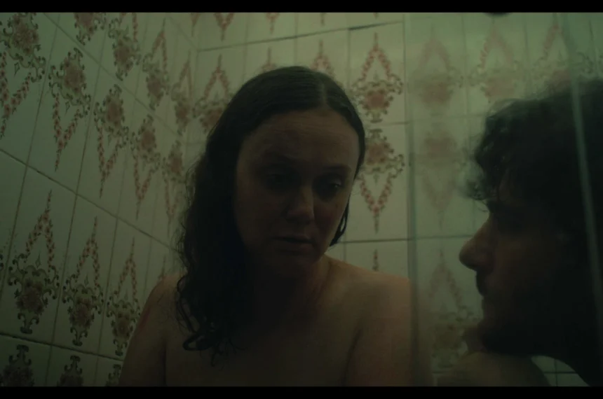 Daniel Tonsig e Anna Zanetti em cena de atrito e tensão no banheiro com iluminação esverdeada e doentia.