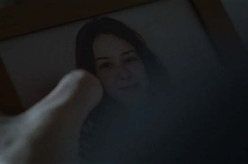 Mão em primeira pessoa segurando um porta-retrato com a foto da personagem da namorada, interpretada por Giovana Telles.